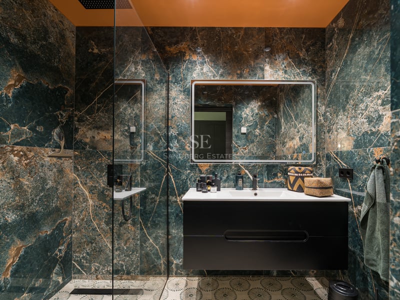 Salle de bain moderne avec carrelage effet marbre vert, meuble vasque noir et grand miroir éclairé.