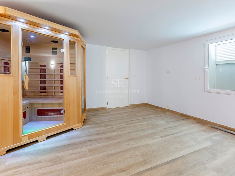 Pièce moderne avec cabine de sauna en bois clair, portes vitrées et sol en grès cérame imitation bois.