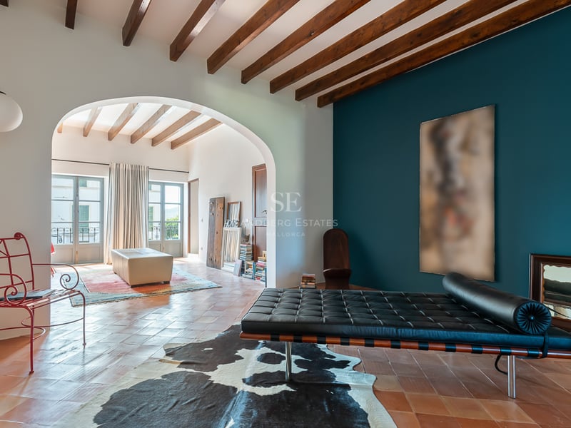 Interior living room with terracotta tiles, exposed ceiling beams, a teal accent wall, and a black leather daybed.