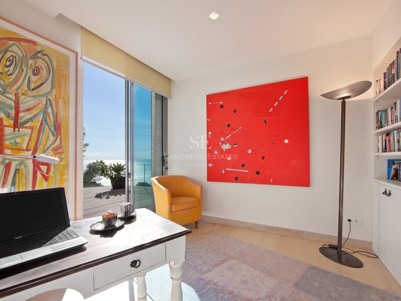 Bureau lumineux avec fauteuil jaune, art abstrait et baies vitrées donnant sur une terrasse face à la mer.
