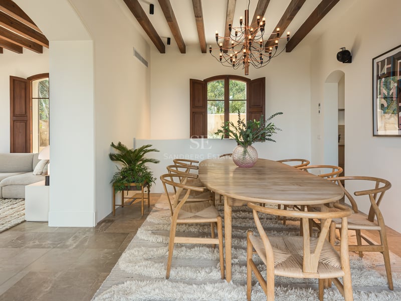 Salle à manger avec table ovale en bois, chaises style Wishbone, tapis en laine et plafond à poutres apparentes.