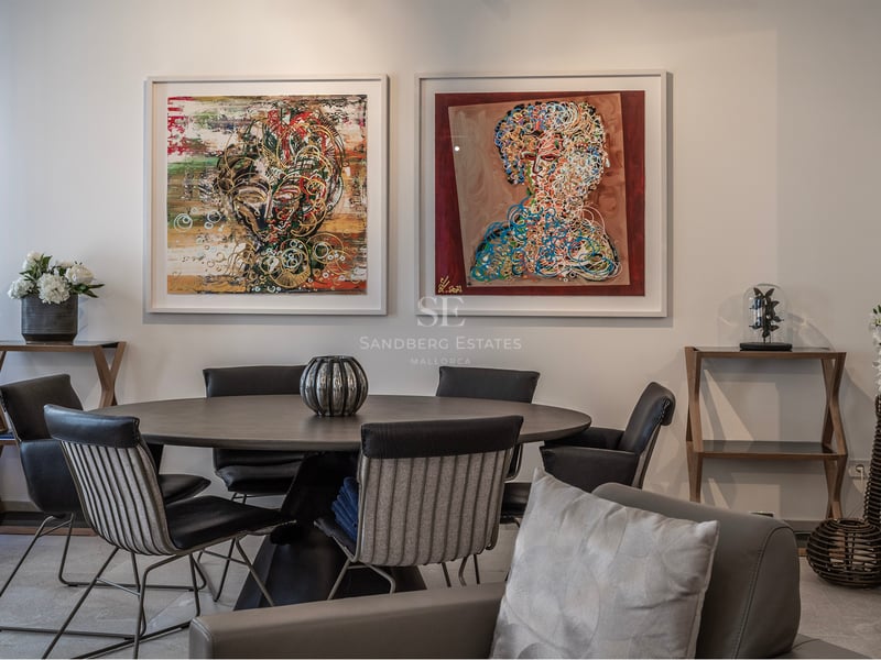Salle à manger moderne avec table ronde sombre, chaises design et deux grands tableaux abstraits au mur blanc.