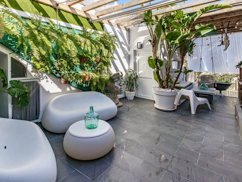 Terrasse extérieure avec canapés blancs arrondis, plantes luxuriantes, sol en pierre grise et pergola en bois.