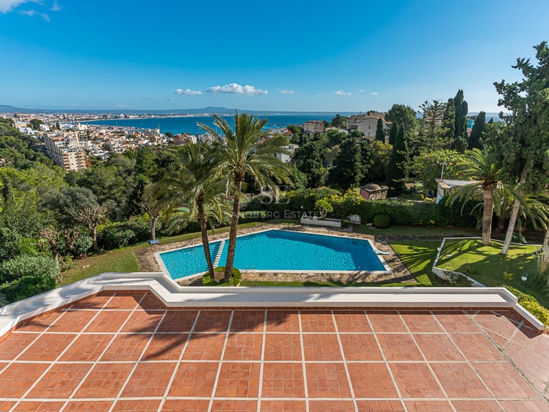 Vue de la piscine à débordement et de la villa moderne minimaliste. De larges fenêtres reflètent le ciel. Design élégant et contemporain.