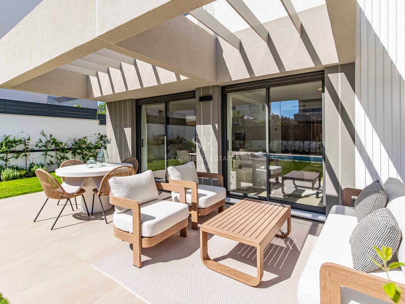 Terrass med trämöbler och matplats intill en privat trädgård under en modern pergola.