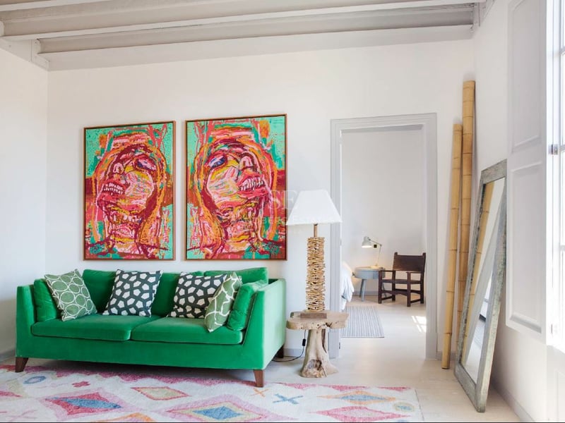 Sala de estar luminosa con sofá de terciopelo verde, dos grandes cuadros coloridos y techos altos con vigas.