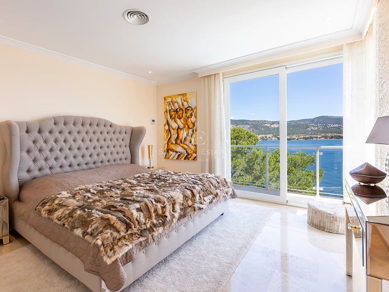 Chambre élégante avec grand lit, tête de lit capitonnée, sol en marbre et baies vitrées offrant une vue sur la mer.