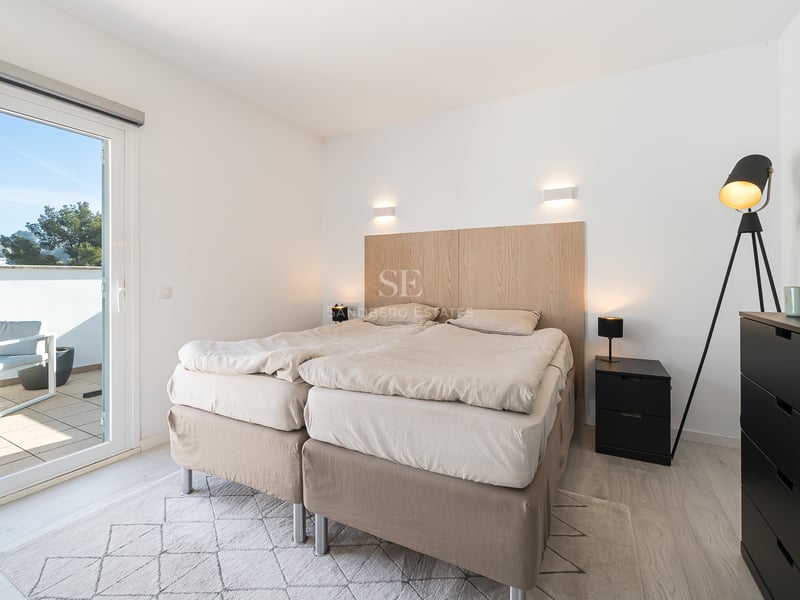 Chambre lumineuse avec un lit double, une tête de lit en bois clair et une baie vitrée ouvrant sur une terrasse ensoleillée.