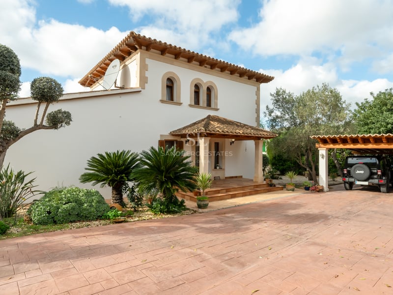 Villa blanche à deux étages avec toit en terre cuite, fenêtres cintrées et une large allée avec parking couvert.