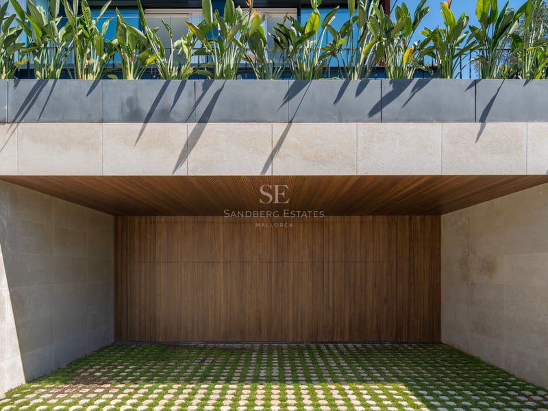 Entrée de garage contemporaine avec porte en bois à lattes, murs en pierre naturelle et pavés drainants végétalisés.