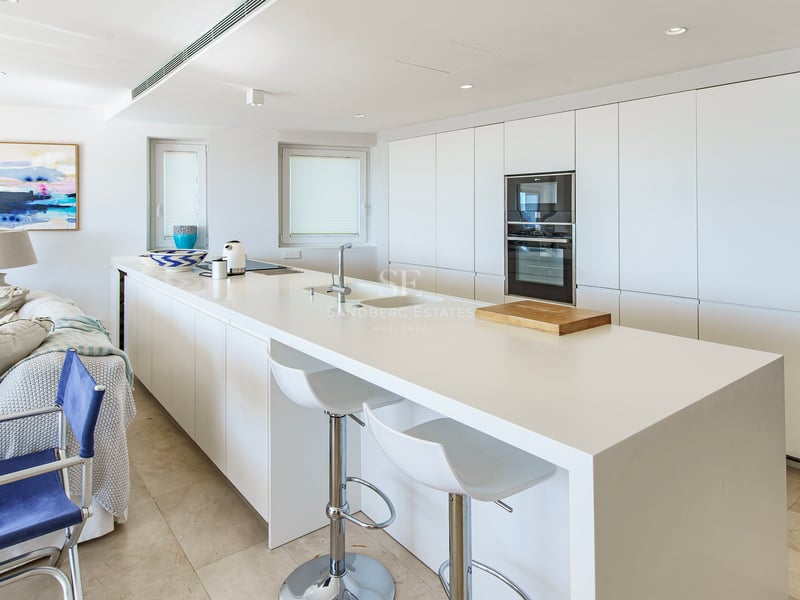 Une cuisine blanche moderne et lumineuse avec un grand îlot central, des tabourets et des appareils intégrés.