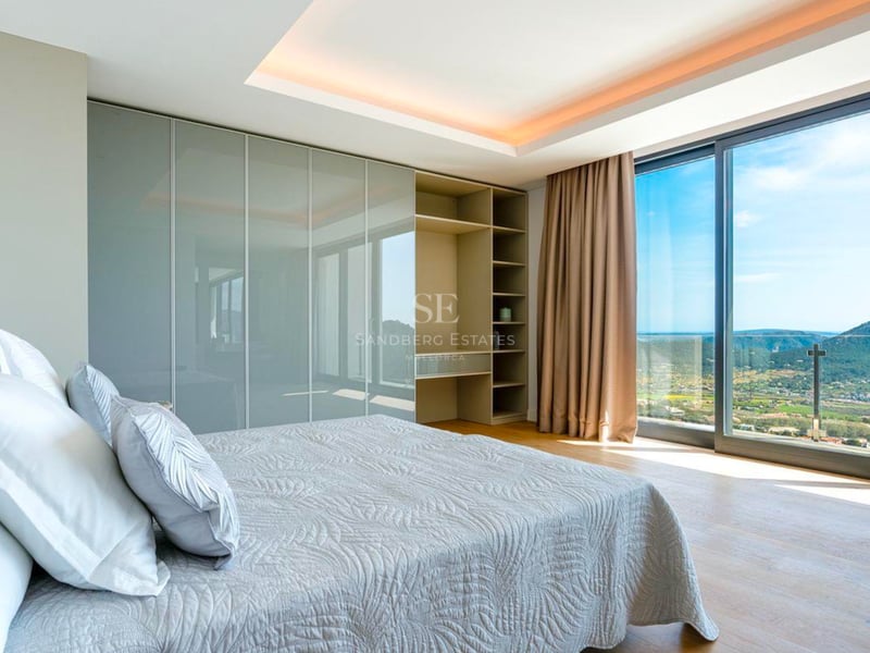 Chambre moderne avec baies vitrées donnant sur la côte, placards intégrés et parquet en bois.