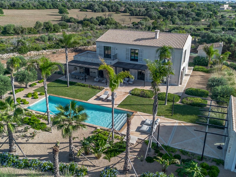 Vue aérienne d'une villa de luxe avec piscine turquoise, palmiers et jardins paysagers.