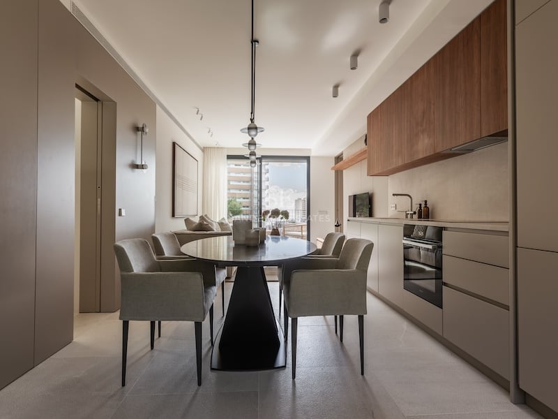 Salle à manger contemporaine avec table ovale noire, fauteuils gris et cuisine minimaliste épurée.