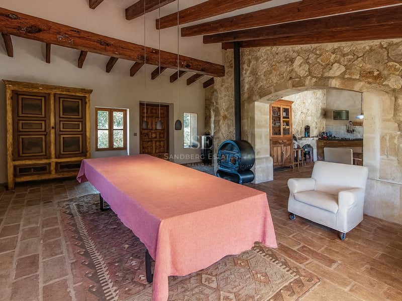 Grande table nappée de rose dans une pièce rustique avec poutres apparentes, murs en pierre et poêle à bois.