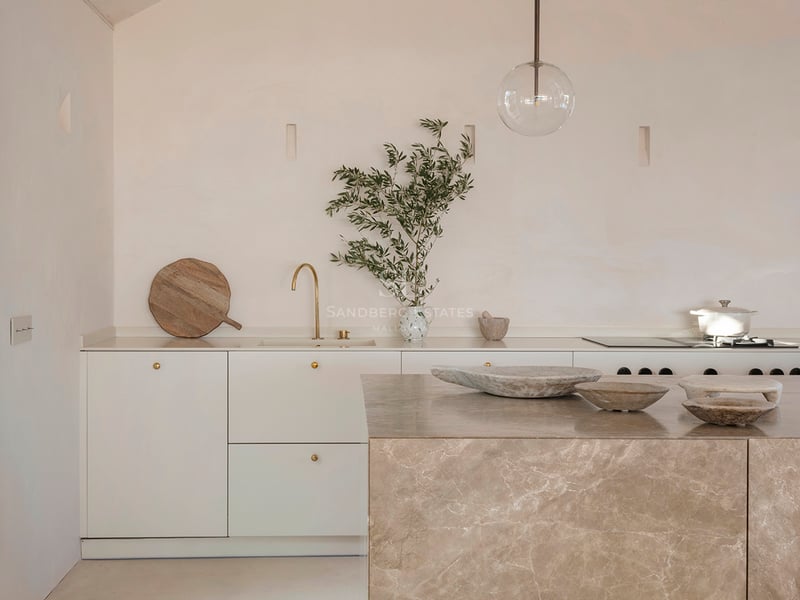 Minimalist kitchen with a large marble island, brass fixtures, and a textured vaulted ceiling in sand tones.