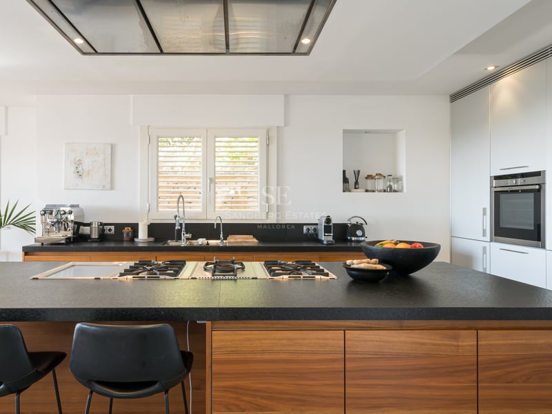Cuisine contemporaine dotée d'un grand îlot en pierre noire, plaques de cuisson au gaz, menuiserie en noyer et meubles blancs.
