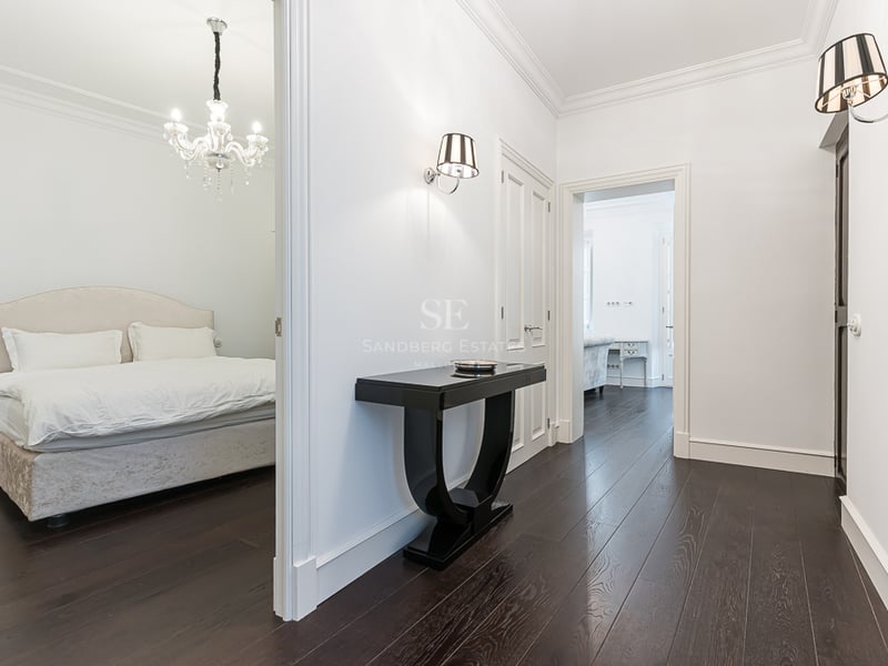 Couloir lumineux avec parquet foncé, console noire et vue sur une chambre avec lustre en cristal.