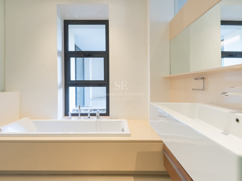 Salle de bain moderne avec une baignoire blanche encastrée près d'une fenêtre et une grande vasque rectangulaire.