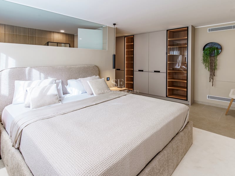 Chambre principale moderne avec grand lit rembourré, armoires encastrées avec éclairage LED et décor neutre.