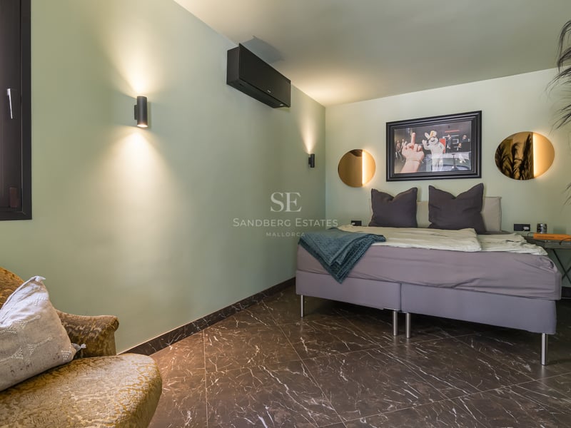 Chambre avec murs vert sauge, sol en marbre sombre, lit gris, fauteuil en velours et miroirs ronds.