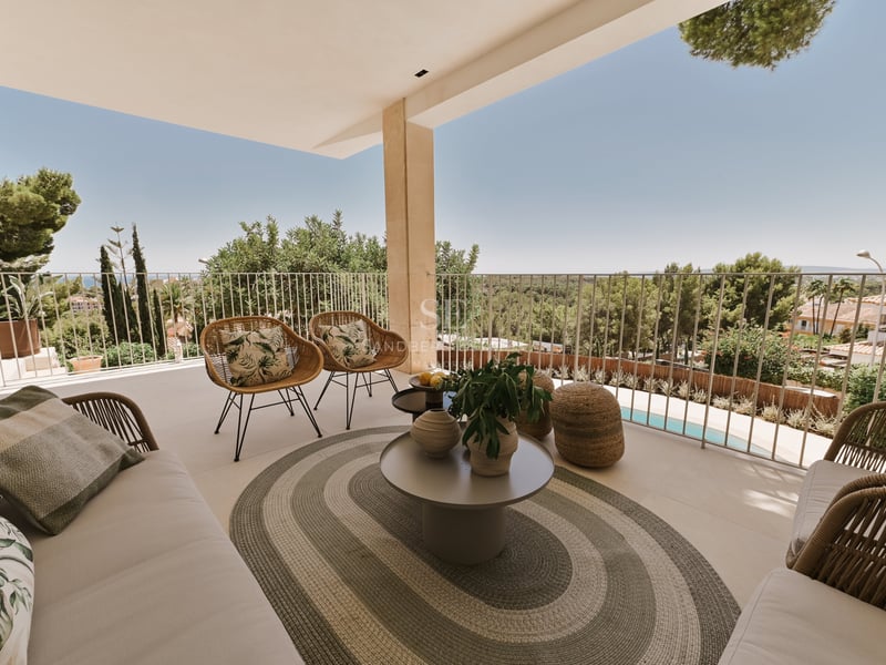 Terrasse en pierre couverte avec fauteuils en osier, tapis ovale et table ronde surplombant un parc et une piscine.