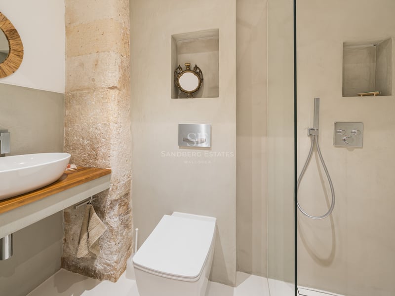Salle de bain moderne avec vasque blanche, plan en bois, pilier en pierre et douche vitrée.