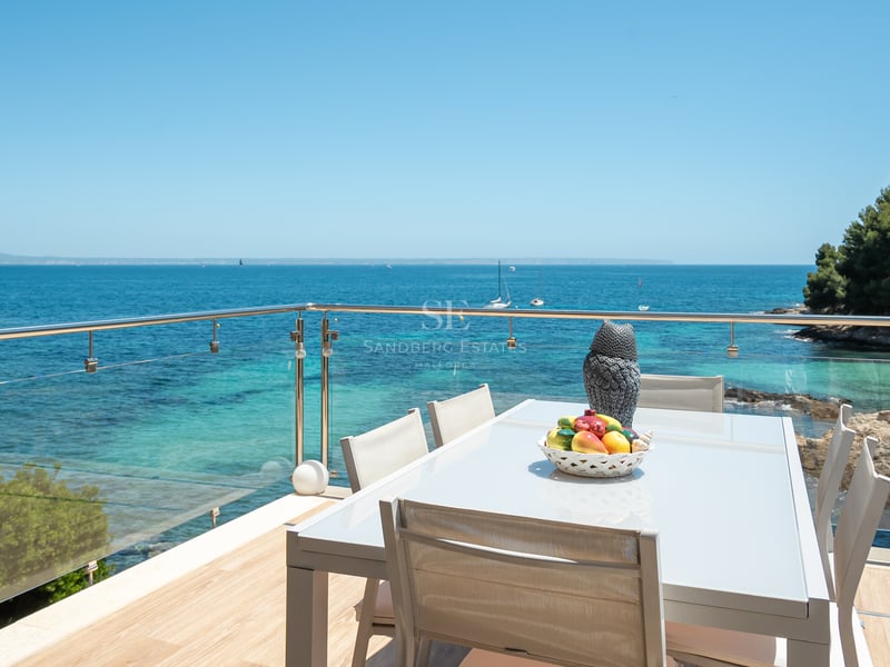 Espace dînatoire extérieur moderne sur une terrasse avec garde-corps en verre surplombant une baie turquoise.