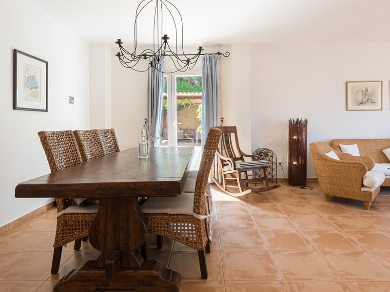 Salle à manger avec table en bois massif, chaises en osier et sol en terre cuite, s'ouvrant sur un coin salon.