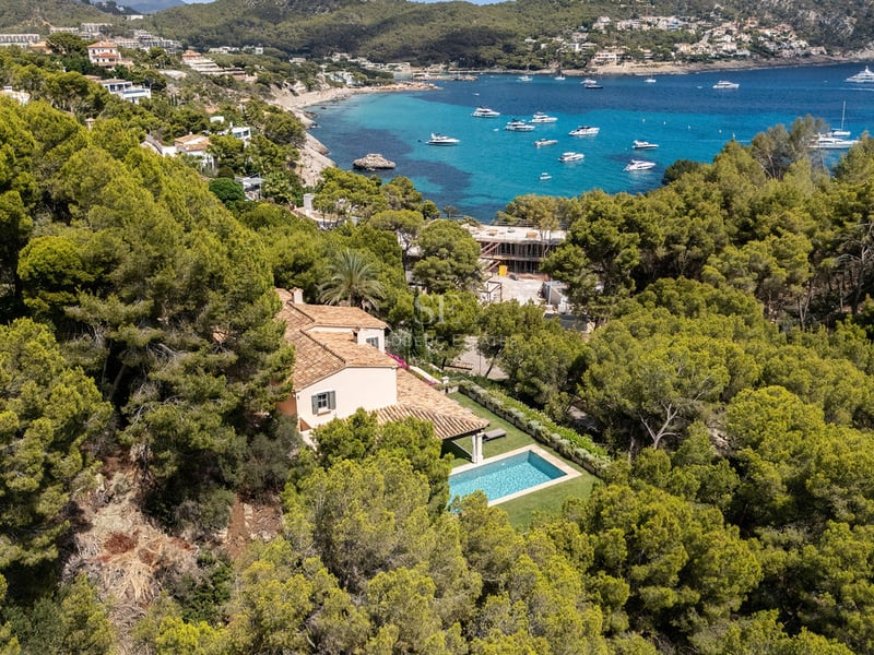 Vue aérienne d'une villa au toit de terre cuite avec piscine privée entourée d'une forêt de pins face à la mer.