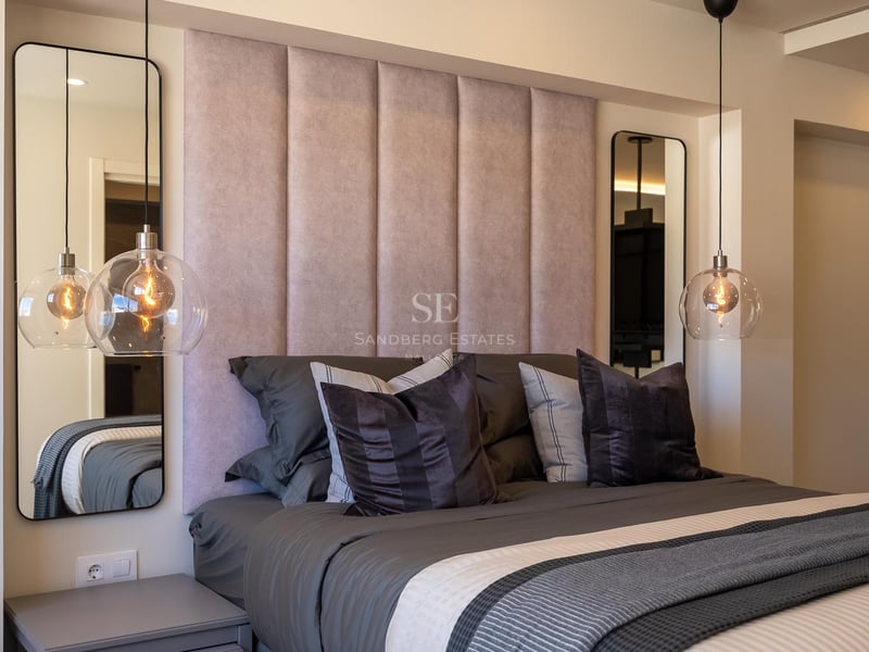 Lit avec tête de lit rose, suspensions en verre et miroirs symétriques dans une chambre de luxe moderne.