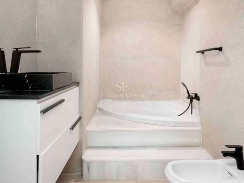 Salle de bain moderne avec baignoire intégrée, marches en marbre blanc et robinetterie noire mate.