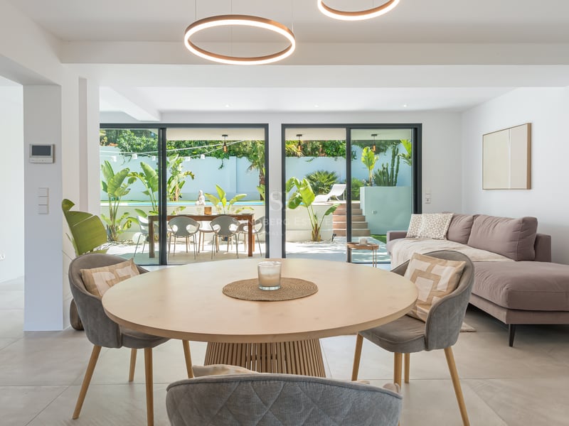 Salon et salle à manger contemporains avec luminaires LED circulaires, canapé gris et vue sur piscine et jardin.