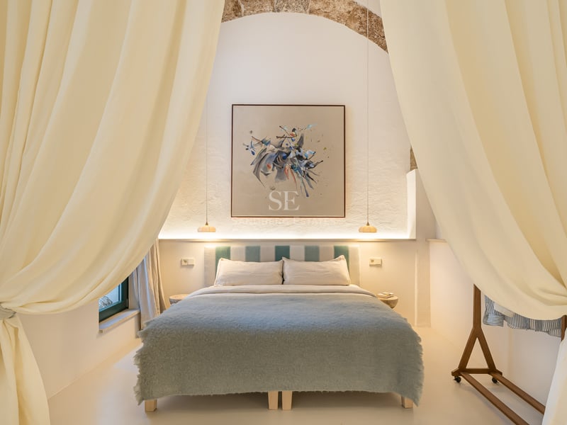 Chambre élégante avec arche en pierre, art abstrait et literie bleu doux encadrée par de grands rideaux crème.