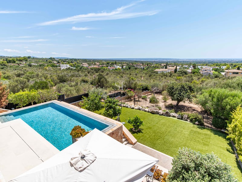 Vue aérienne d'une piscine bleue entourée d'une terrasse en pierre et d'un jardin avec vue sur l'horizon méditerranéen.
