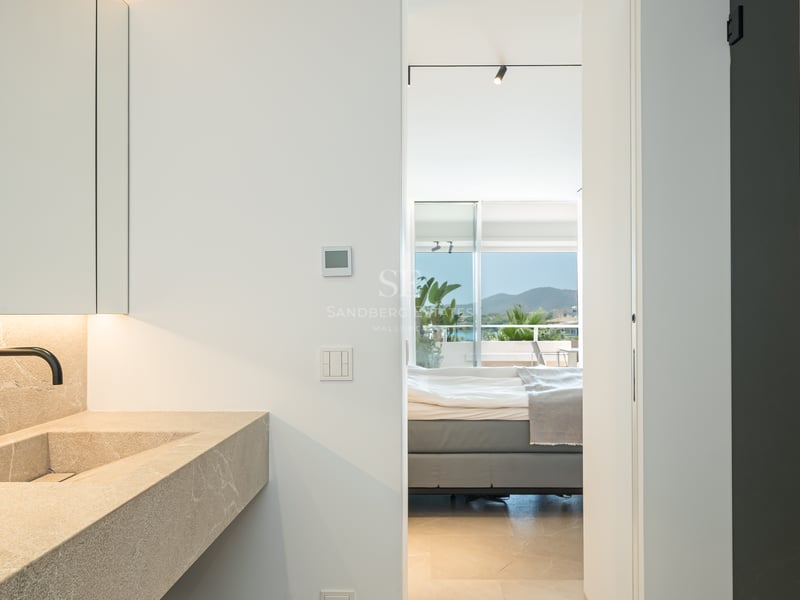 Salle de bain moderne avec vasque en pierre et robinet noir, vue sur la chambre et les montagnes au loin.