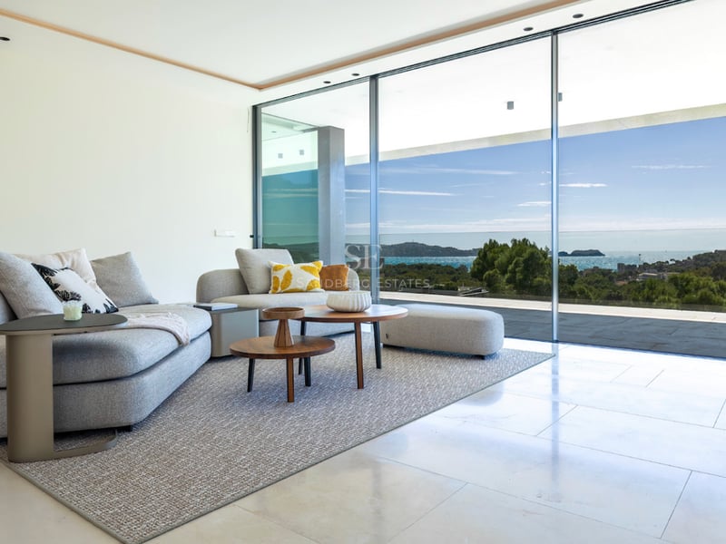 Salon lumineux avec canapé gris, tables en bois et baies vitrées offrant une vue imprenable sur la mer.