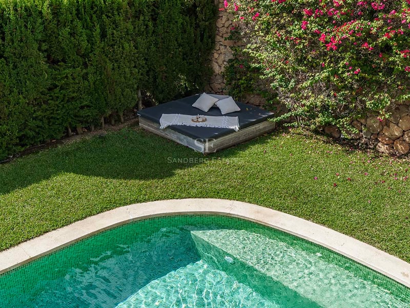 Piscine aux carreaux verts bordée d'une pelouse impeccable et d'un lit de repos sous des bougainvilliers.