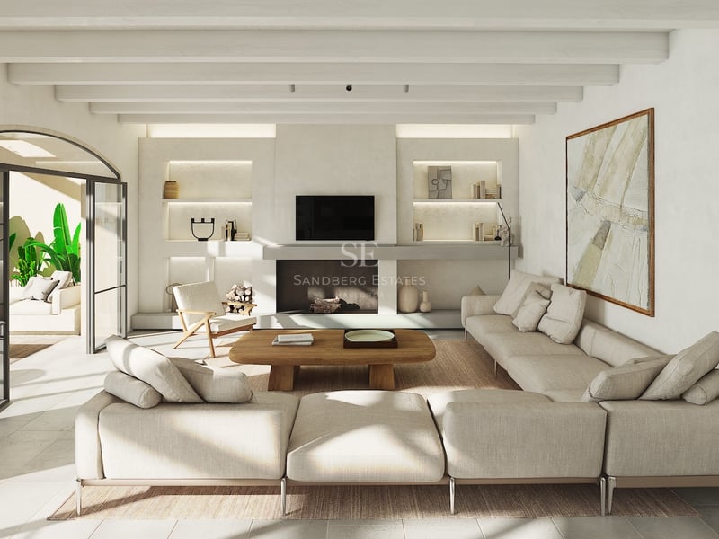 Salón luminoso con sofá modular beige, techos con vigas de madera y salida arqueada a una terraza con plantas.