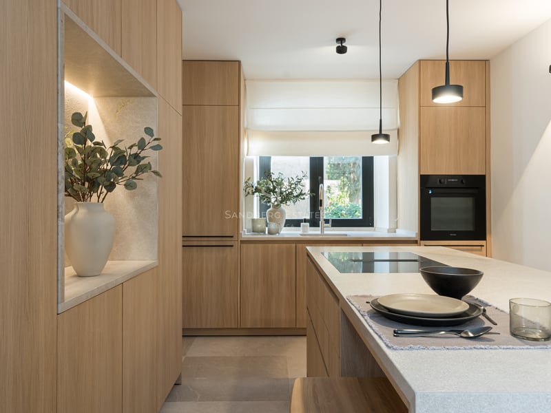 Cuisine moderne avec placards en chêne, îlot en pierre, suspensions minimalistes et niche décorative éclairée.