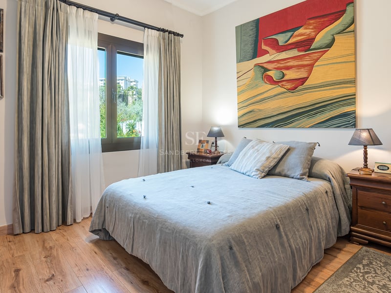 Chambre lumineuse avec parquet, lit aux draps gris, tables de chevet en bois et grand tableau coloré.