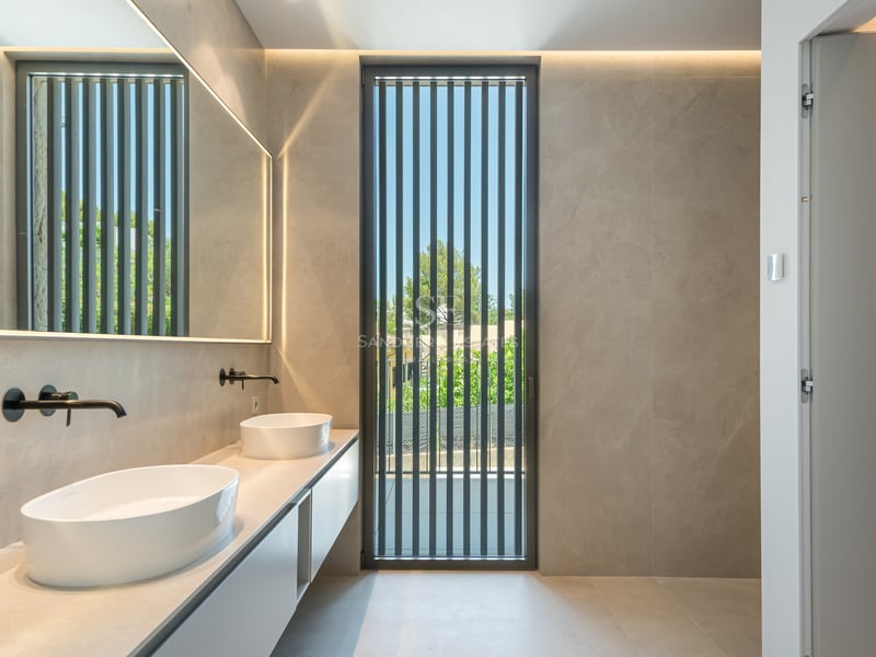 Salle de bain moderne avec double vasque ovale, robinetterie noir mat et grand miroir rétroéclairé.