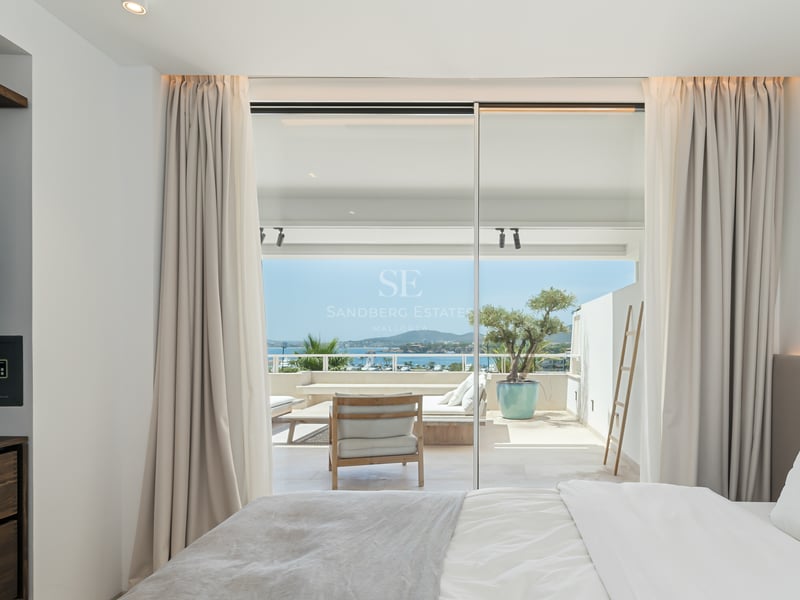 Chambre lumineuse avec baies vitrées s'ouvrant sur une terrasse ensoleillée offrant une vue sur la mer.