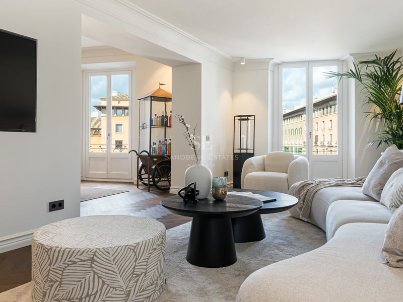Contemporary living room featuring a curved white sofa, black coffee tables, and large windows overlooking urban buildings.