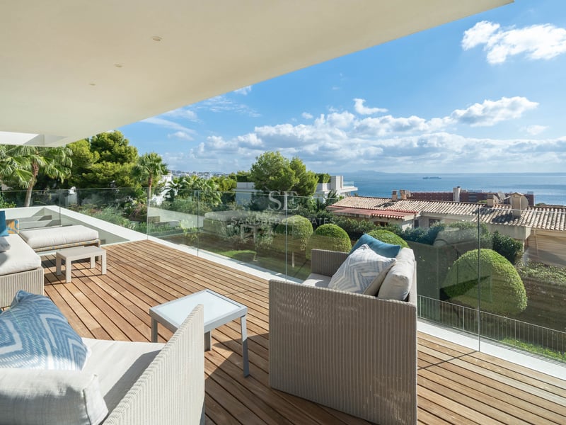 Terrasse moderne avec terrasse en bois, canapés blancs et garde-corps en verre offrant une vue sur mer.