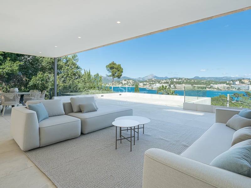 Terrasse couverte contemporaine avec canapés modulaires et coin repas surplombant la mer bleue et la côte.