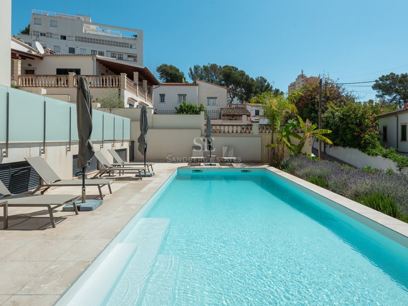 Piscine rectangulaire aux eaux turquoises, terrasse en pierre claire, bains de soleil gris et jardin méditerranéen.