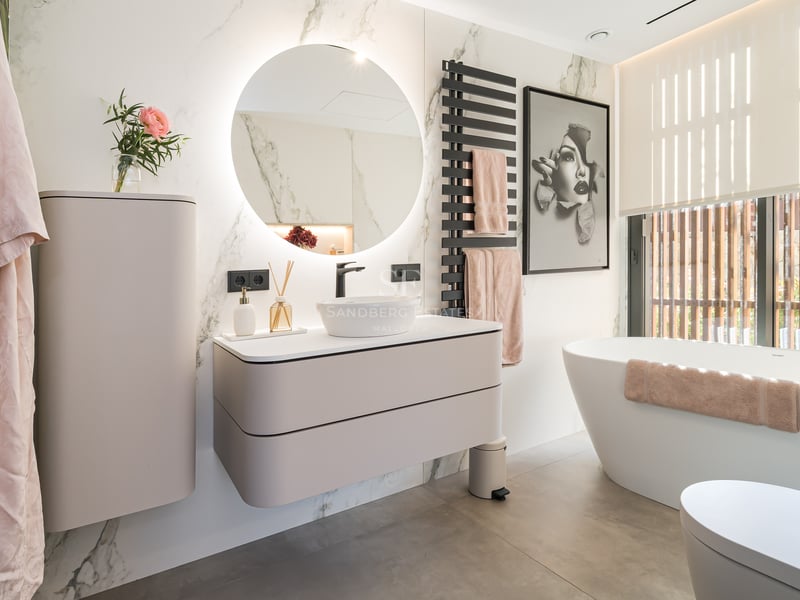 Salle de bain moderne avec miroir rond rétroéclairé, meuble suspendu et baignoire îlot blanche.