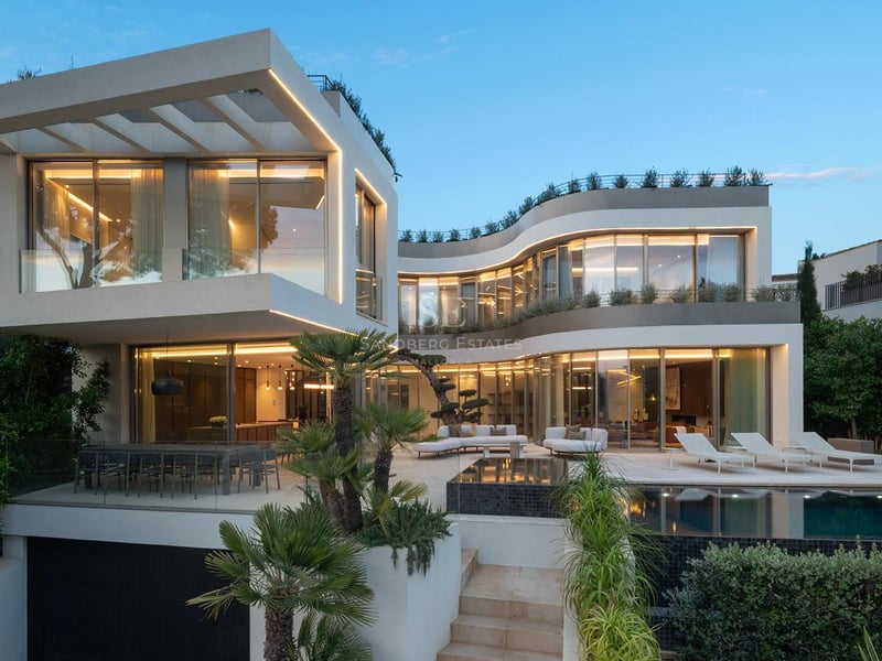 Vue nocturne d'une villa contemporaine à plusieurs niveaux avec façades vitrées courbes, terrasse et piscine éclairée.