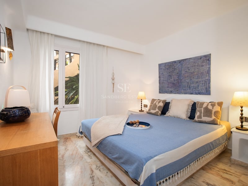 Chambre blanche avec lit bleu, bureau en bois et sol en marbre veiné sous une lumière chaude.